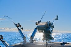 Fishing rods on a boat at sea, bright sunlight, blue water and sky.