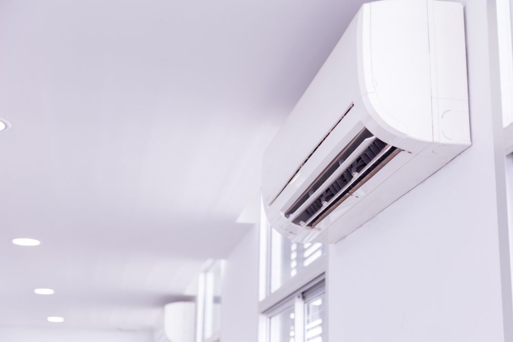 White wall-mounted air conditioning unit in a room with white walls, near a window. — Jade Fluerty Electrical In Tinana, QLD