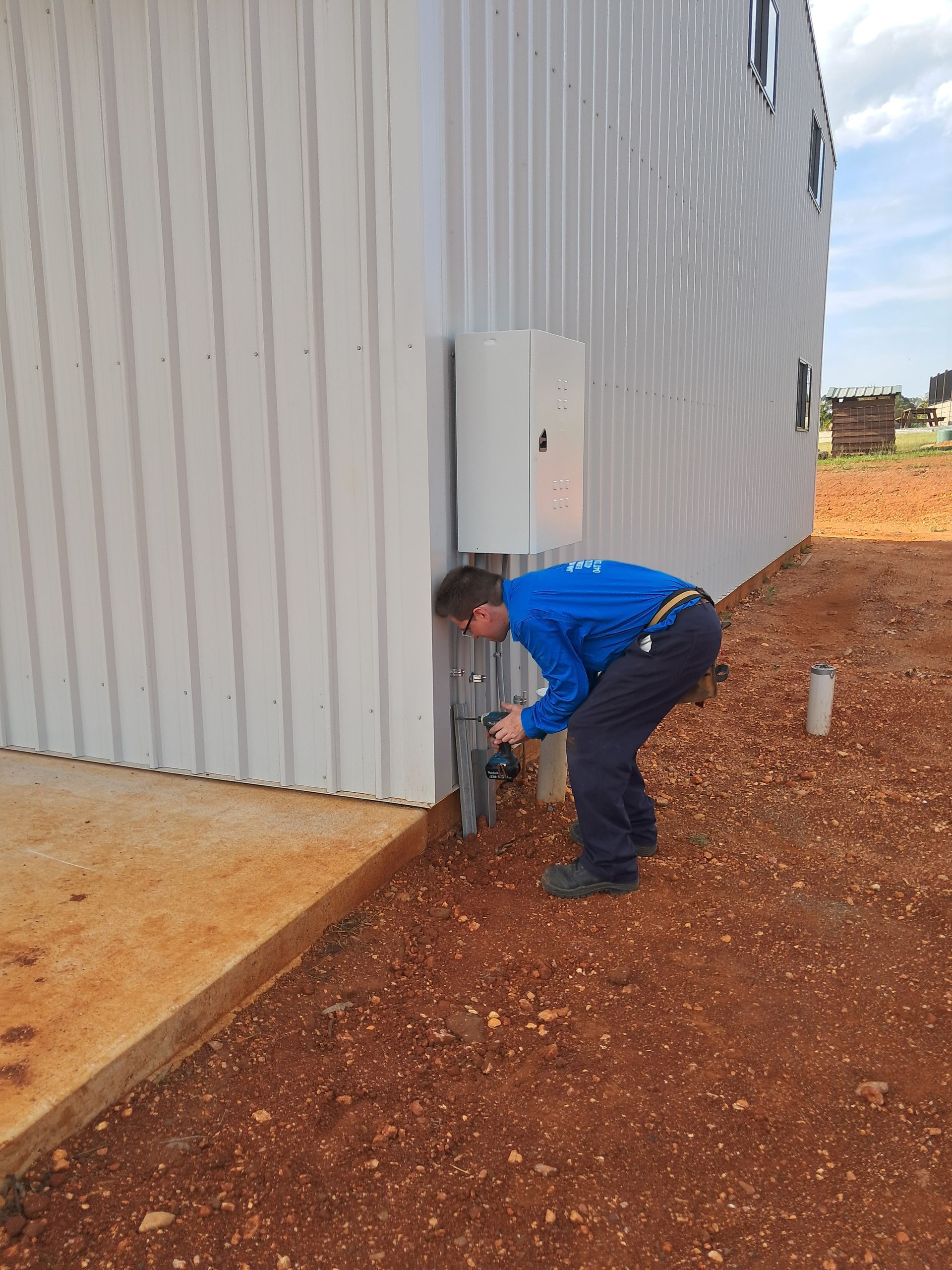 Man in blue shirt working on plumbing near a white building with an electrical box — Jade Fluerty Electrical In Tinana, QLD