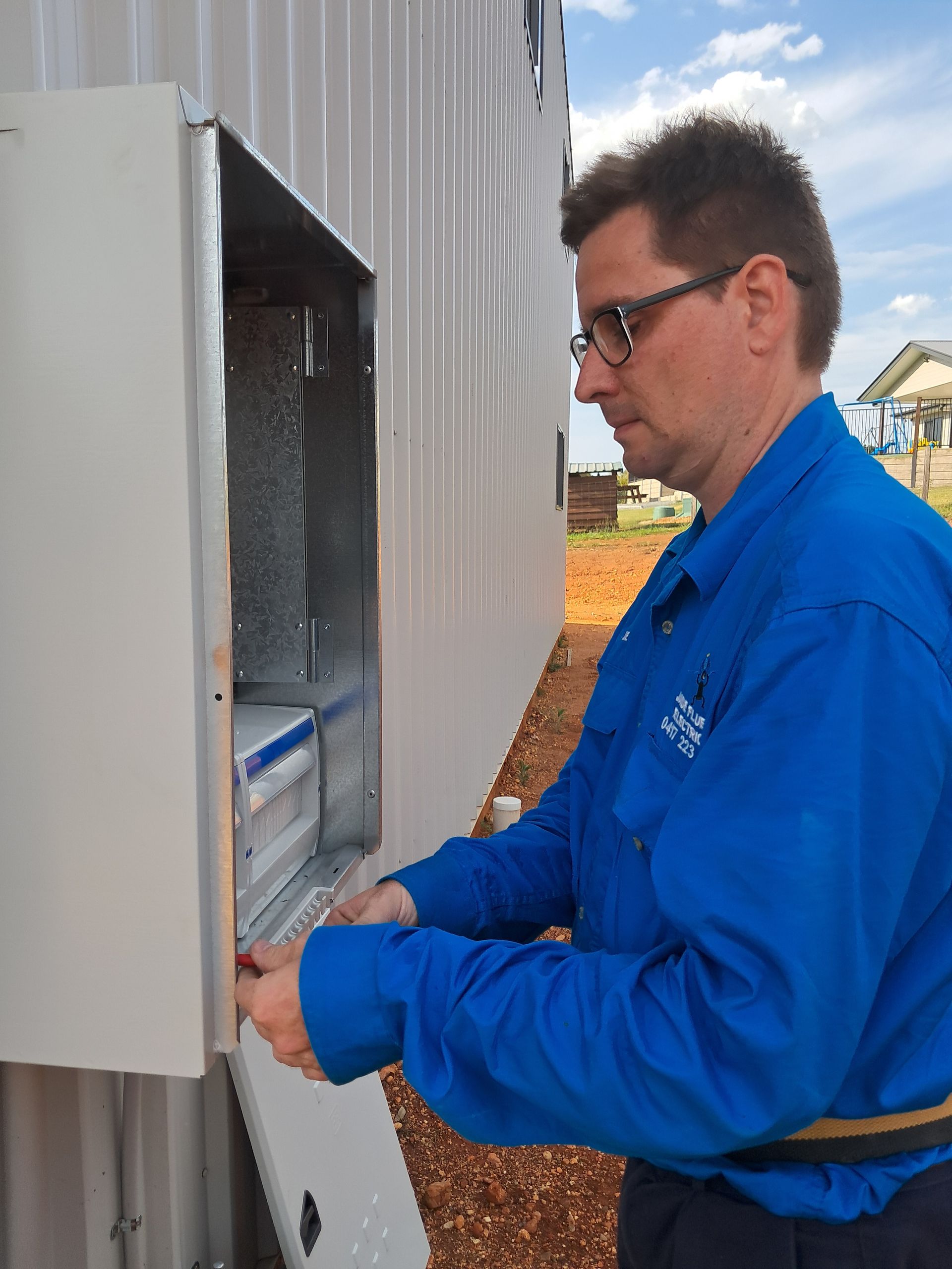 Man in blue work shirt installing a piece of equipment on a building exterior — Jade Fluerty Electrical In Tinana, QLD