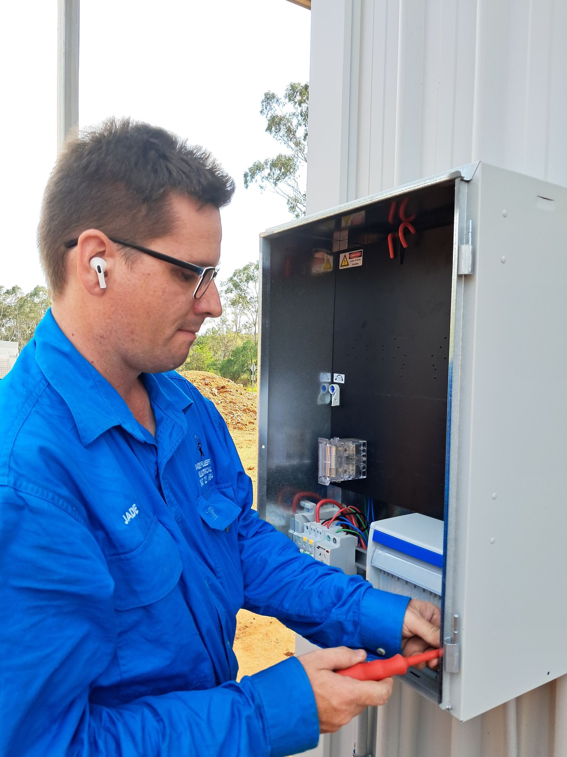 Electrician in a blue shirt works on an electrical panel. Outdoor setting, using a tool — Jade Fluerty Electrical In Tinana, QLD