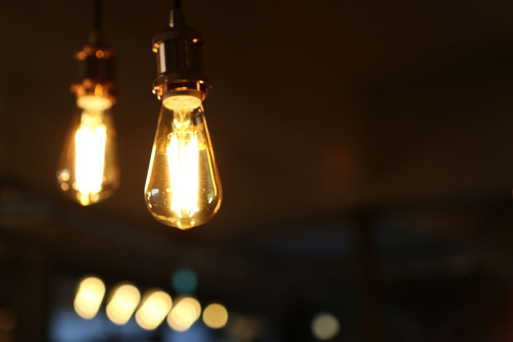 Two lit Edison light bulbs hanging from ceiling, warm glow, dark background — Jade Fluerty Electrical In Tinana, QLD