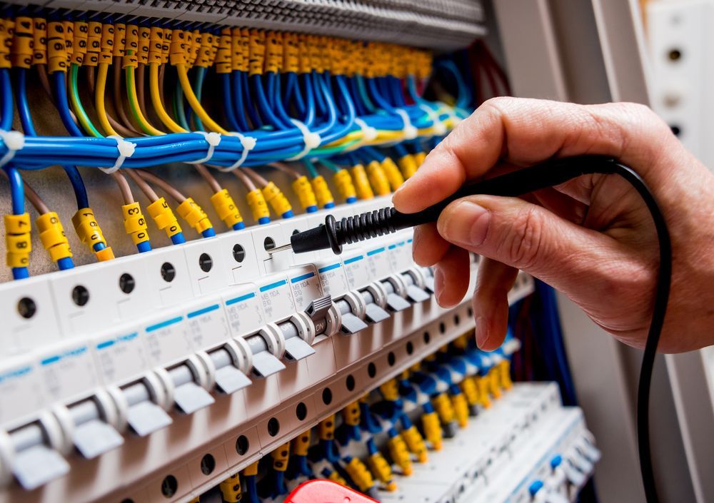 Hand Testing Electrical Panel With a Probe; Colorful Wires and Switches — Jade Fluerty Electrical In Tinana, QLD