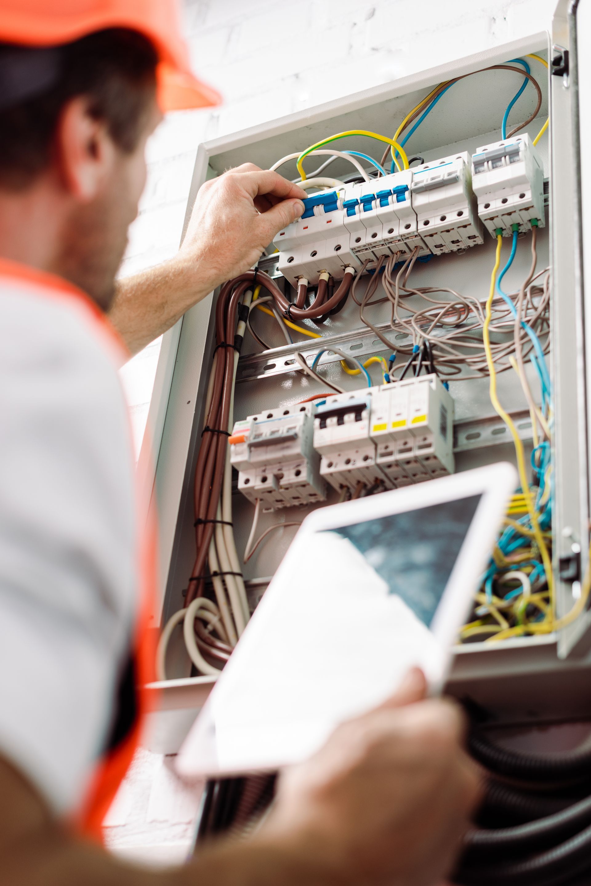 An electrician is working on an electrical box and looking at a tablet.
