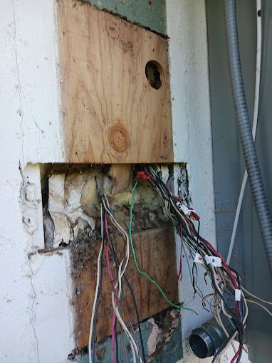 A bunch of wires are coming out of a hole in a wall.