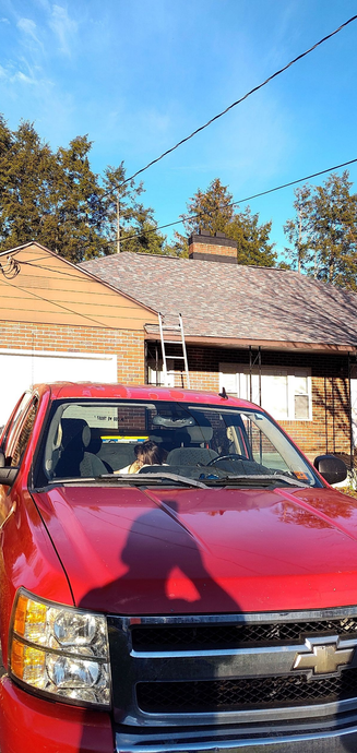 A red pickup truck is parked in front of a house undergoing roof repairs, with a ladder leaning against the structure.