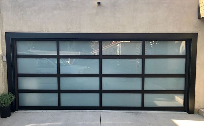 A black garage door with frosted glass is sitting on a concrete driveway.
