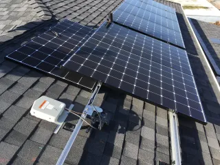 Solar panels mounted on a shingled roof with a grey electrical junction box and metal racking visible.