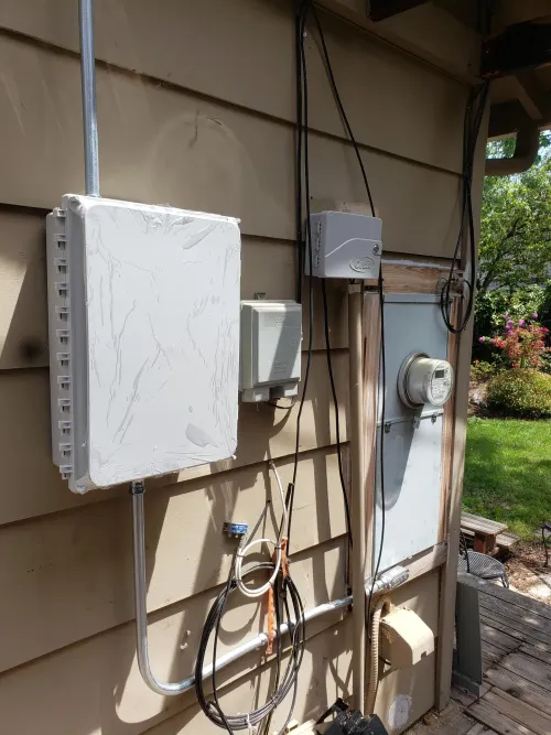 Utility equipment on a tan exterior wall, including a large gray box, smaller junction boxes, and an electrical meter.