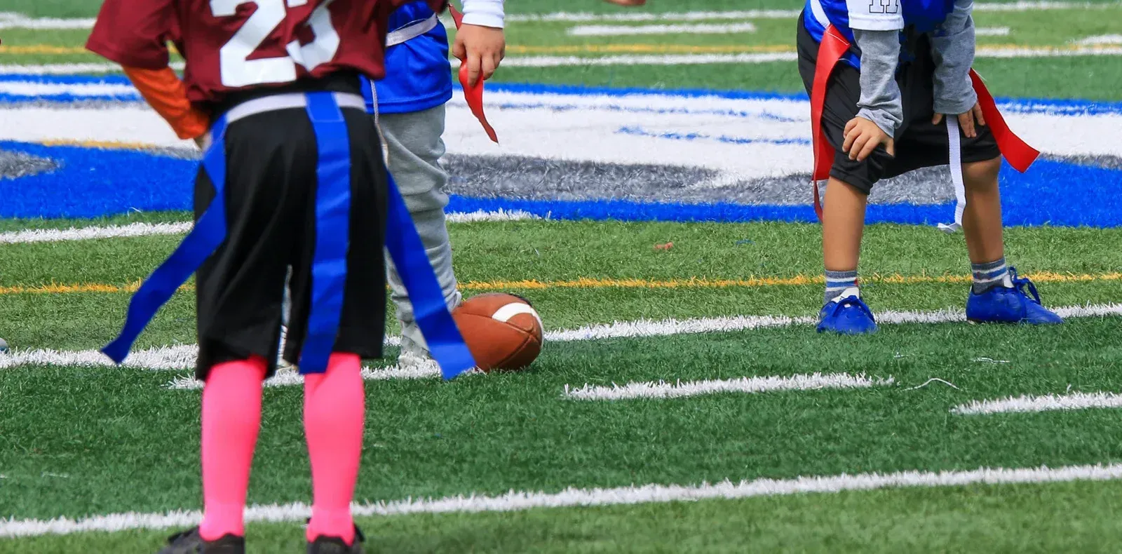 Children playing flag football on a green field, focusing on a football on the ground.