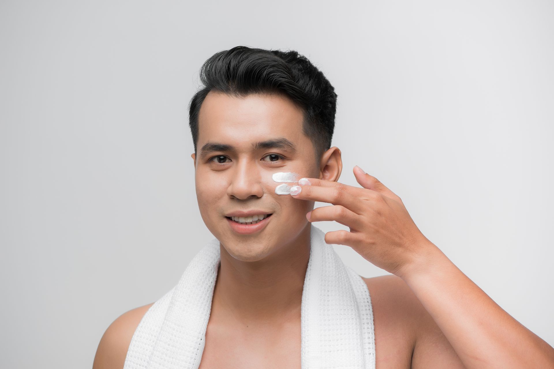 a man with a towel around his neck is applying cream to his face .
