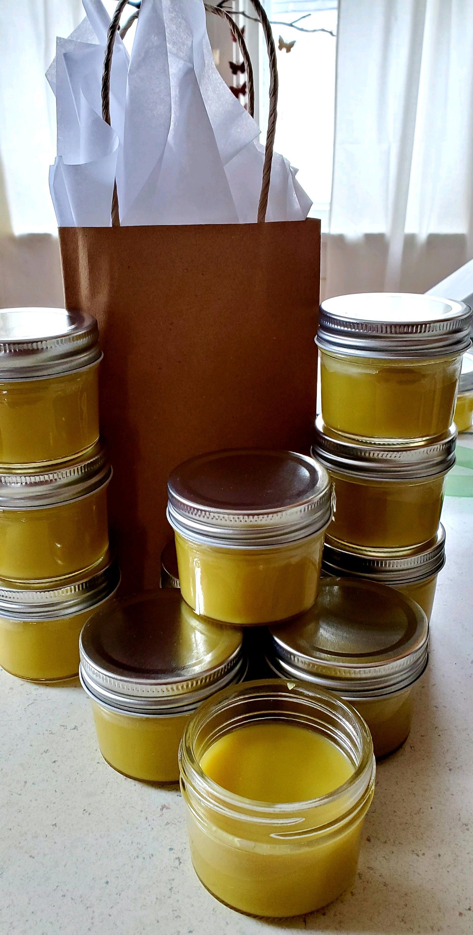 A stack of small glass jars filled with yellow substance, next to a brown gift bag with white tissue paper.