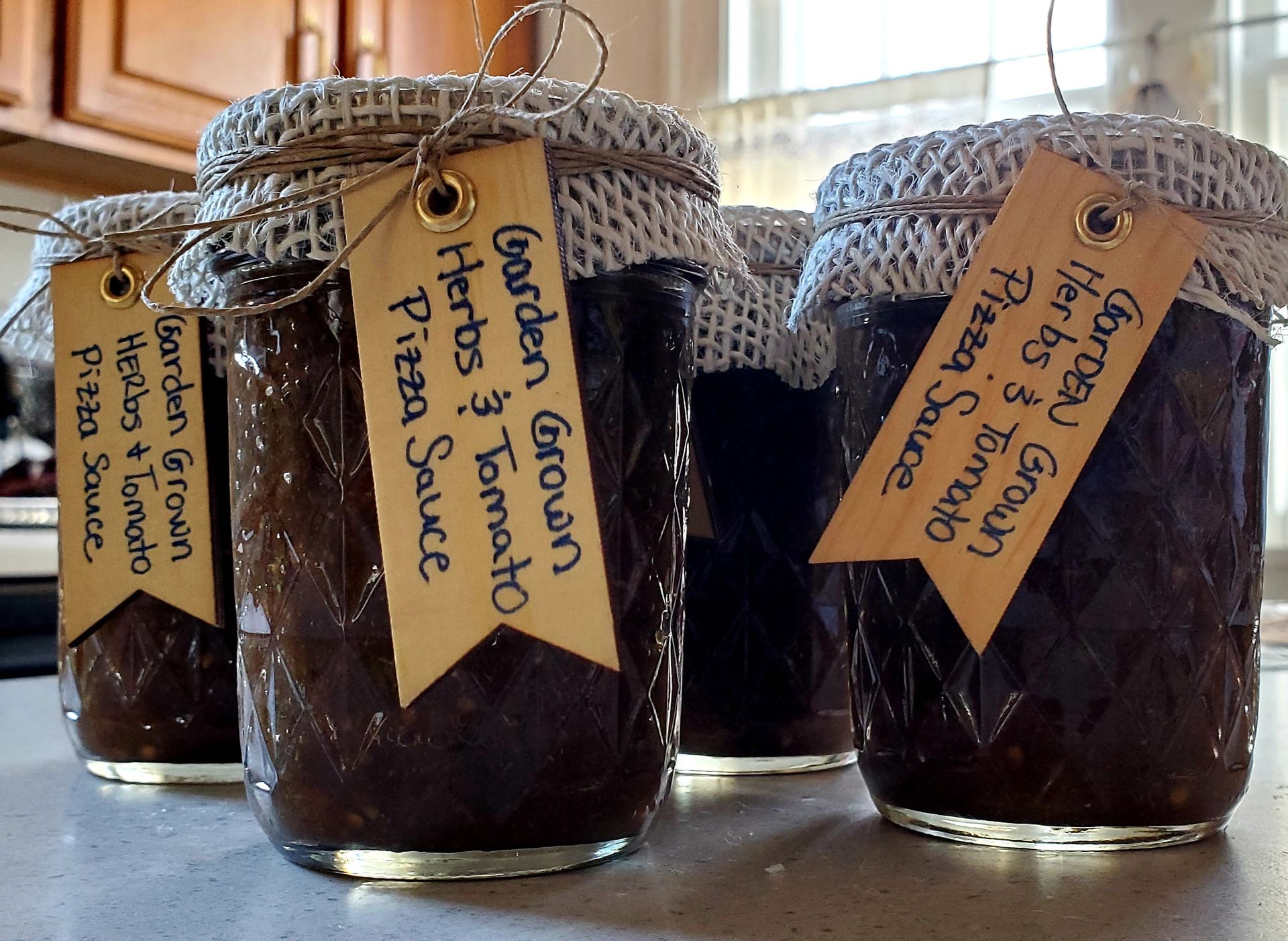 Four glass jars of homemade pizza sauce with tags.