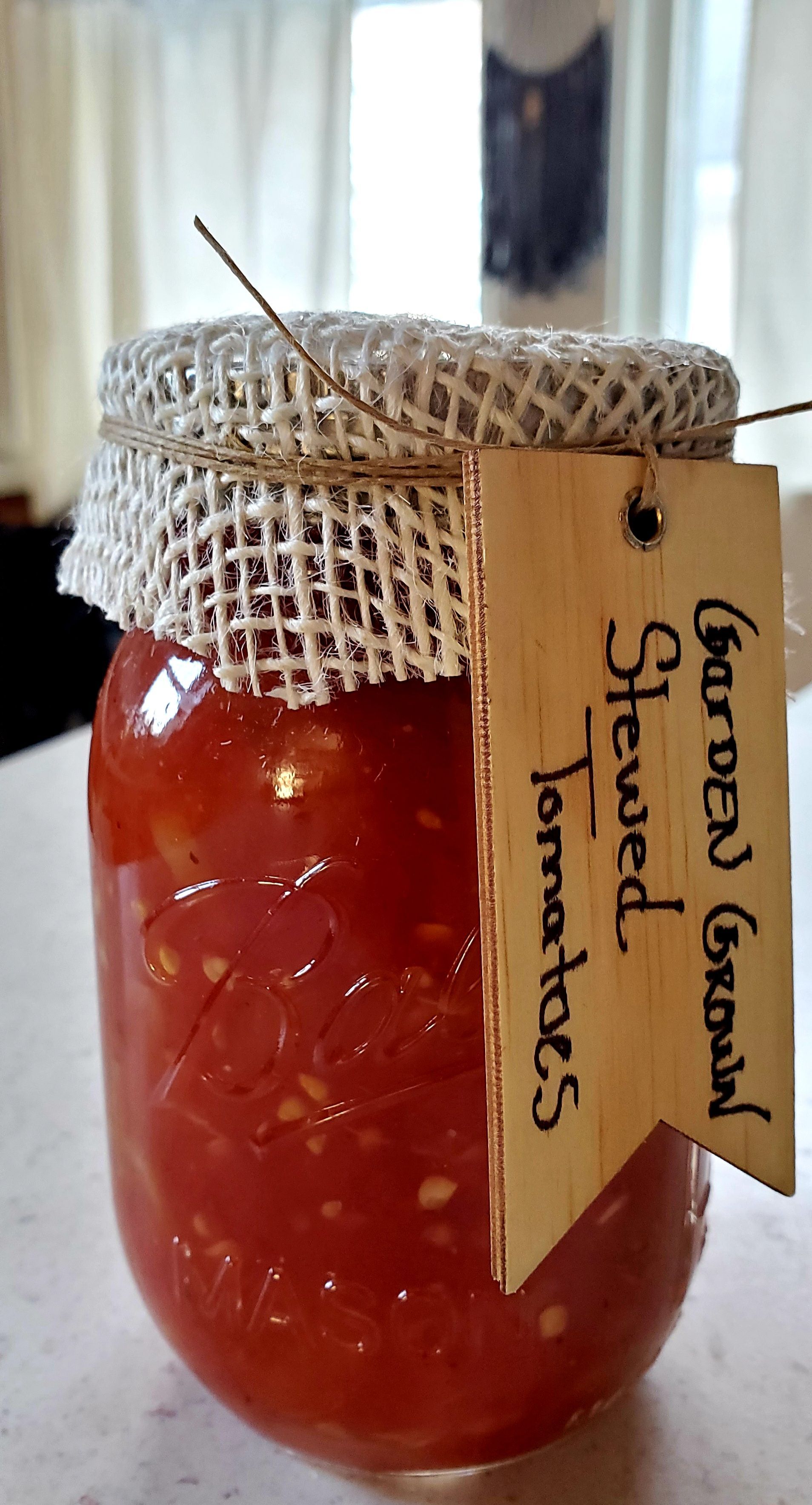 Jar of stewed tomatoes with burlap lid and wooden tag that says