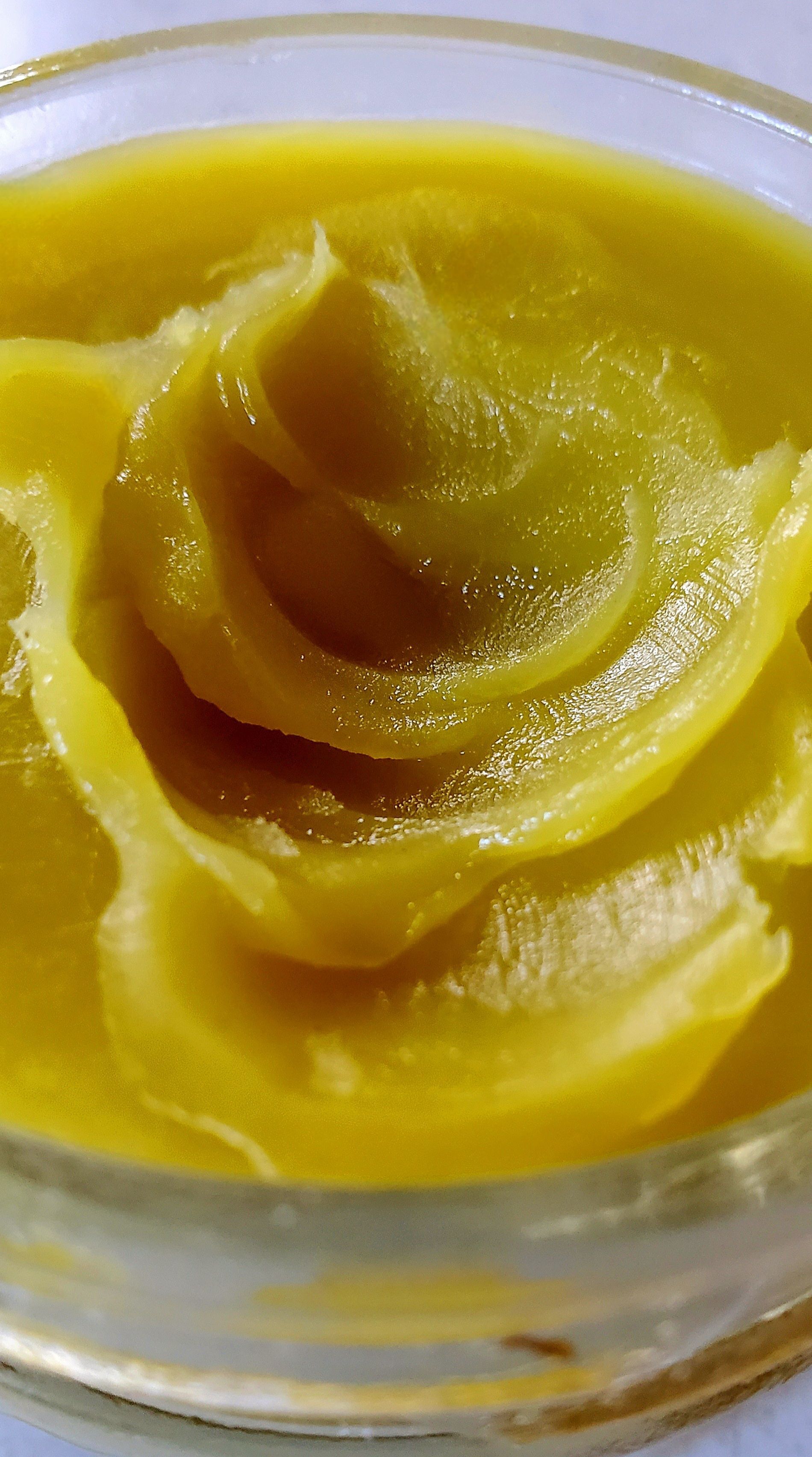 Close-up of a yellowish-green, thick, and swirled substance in a clear glass container.