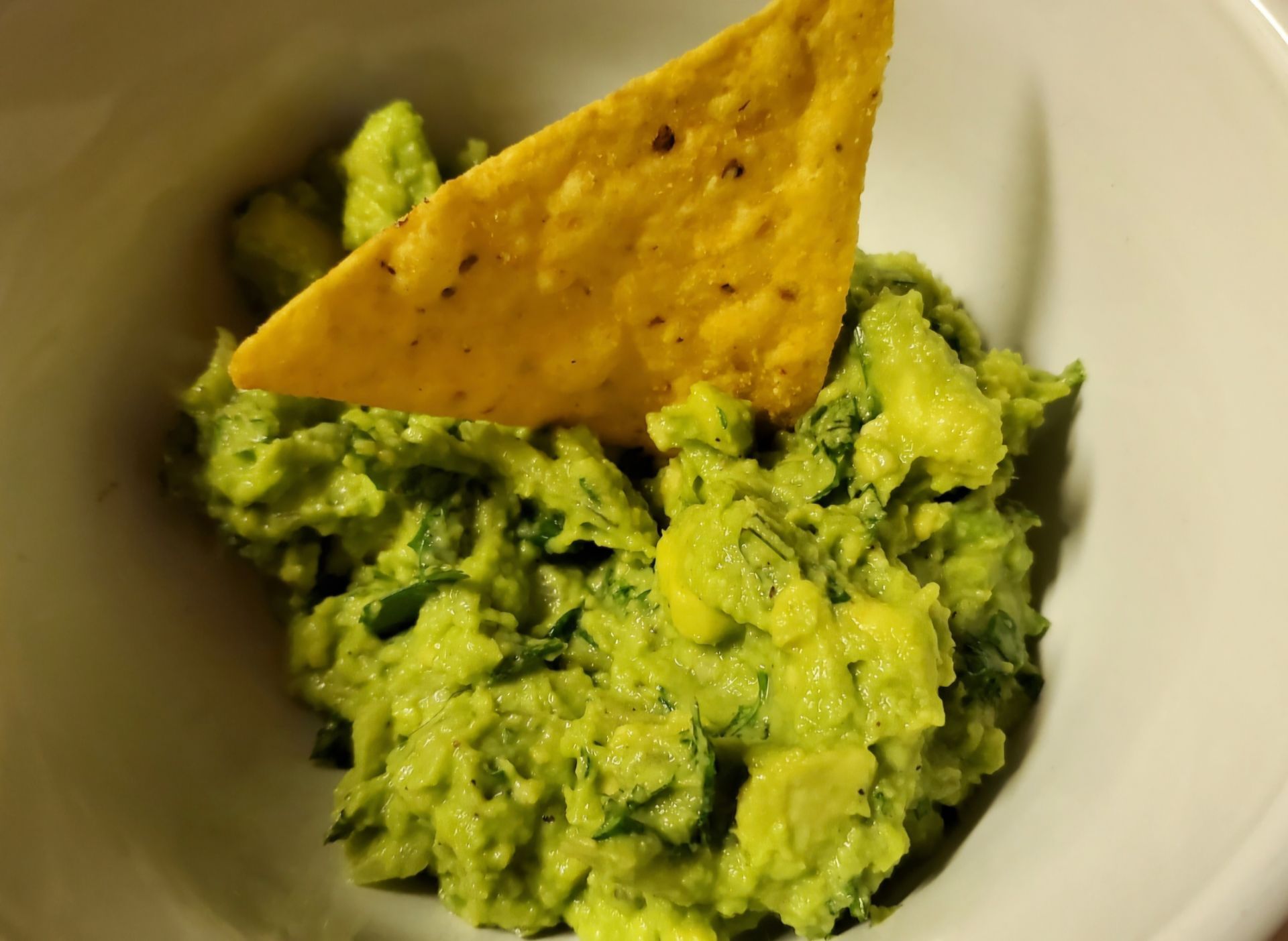 Guacamole with a tortilla chip in a white bowl. The guacamole is bright green.