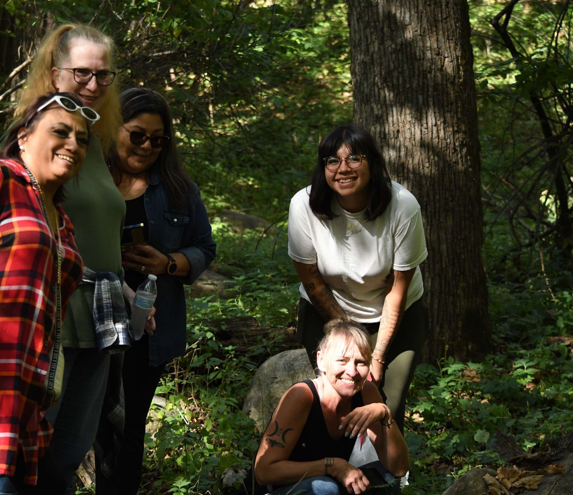 Five people smiling in a sunlit forest. Trees, rocks, and foliage surround them.
