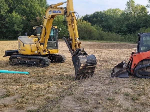 A yellow excavator and a red skid steer are in a field.