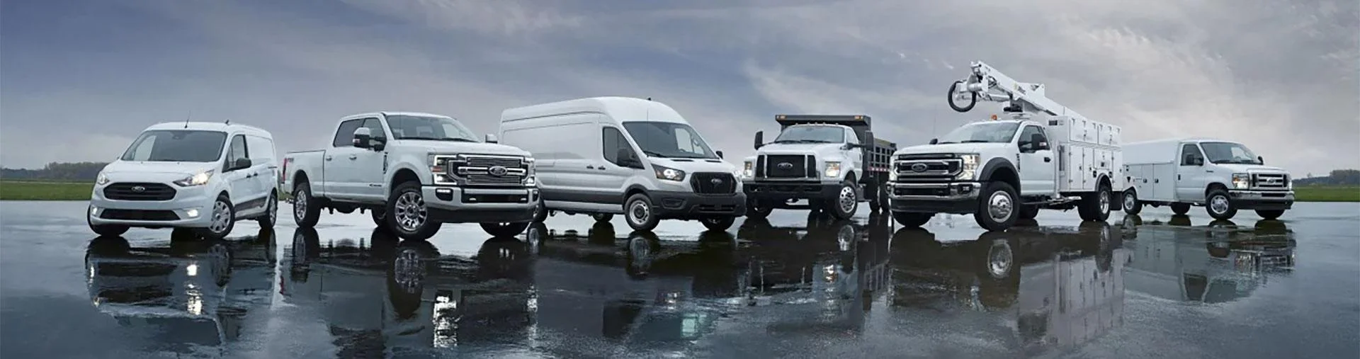 A row of white trucks and vans are parked next to each other on a wet surface.