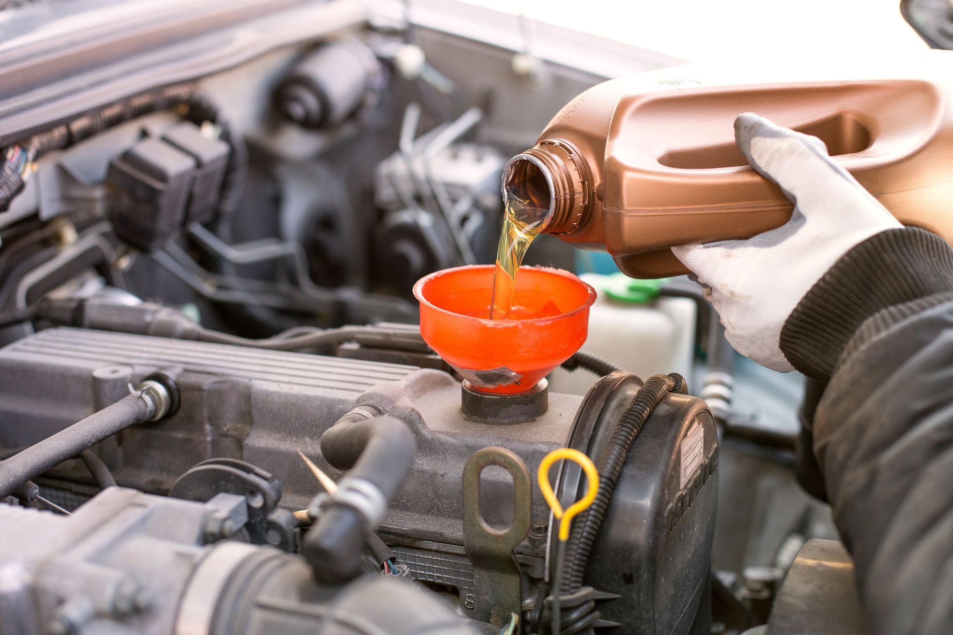 Person pouring motor oil into a car engine using a funnel.