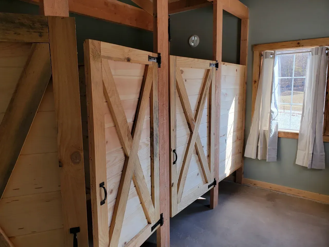 A bathroom with a row of wooden stalls and a window.