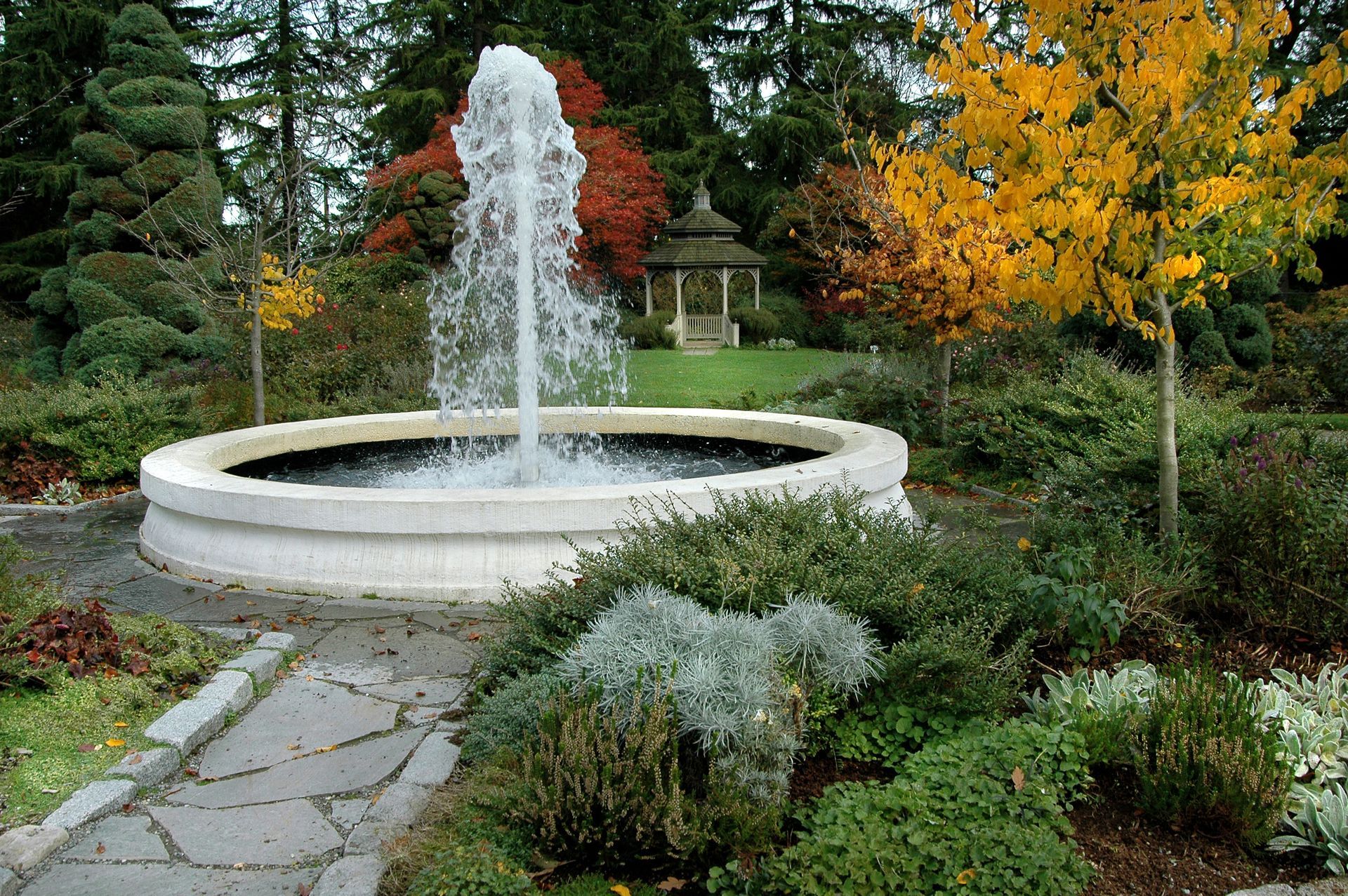A fountain in a garden with a gazebo in the background
