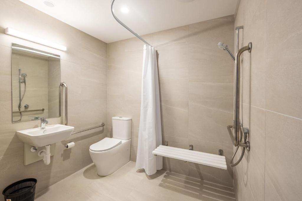 A bathroom with a toilet , sink , shower and bench.