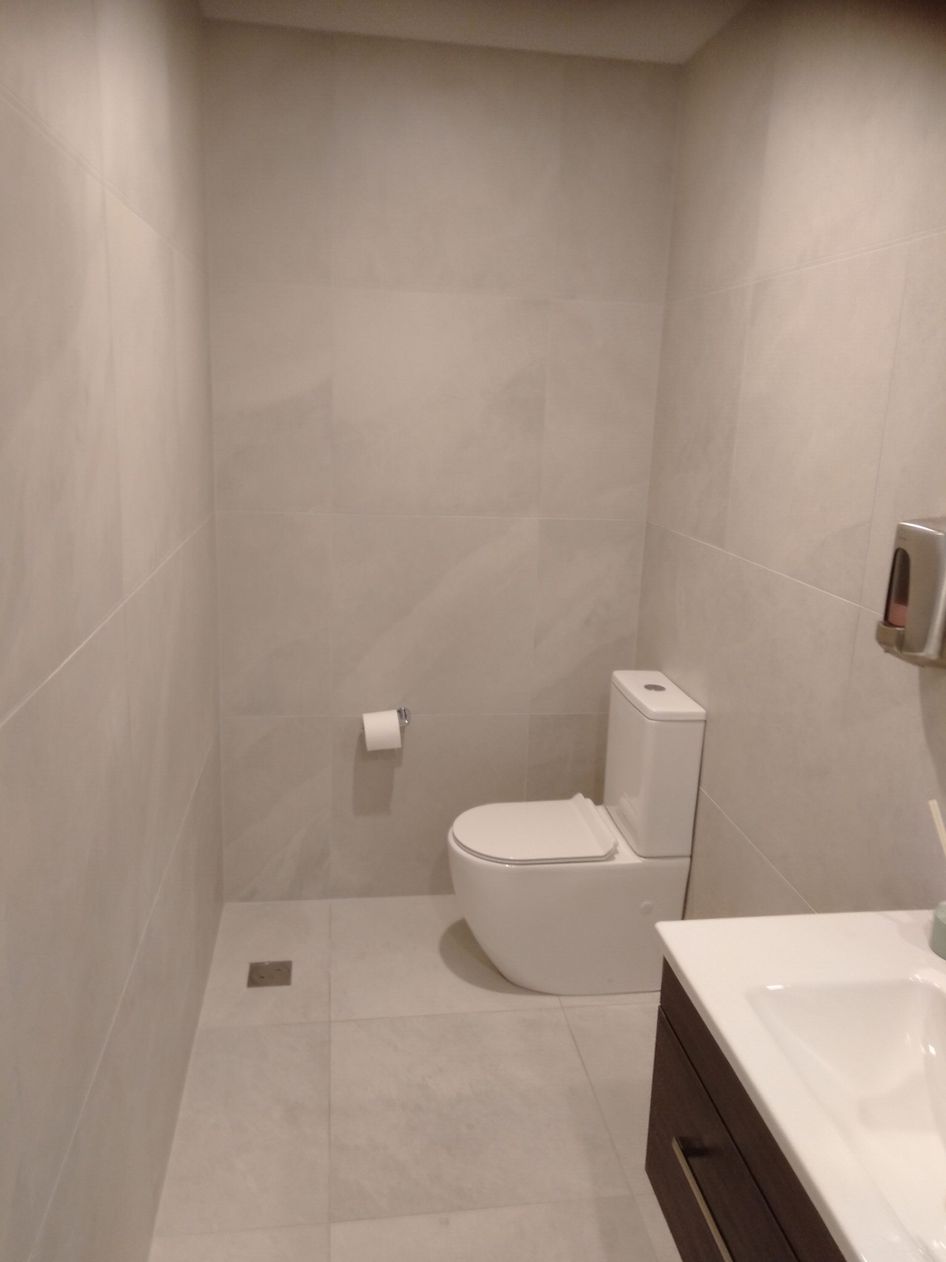 A bathroom with a toilet , sink , and paper towel dispenser.