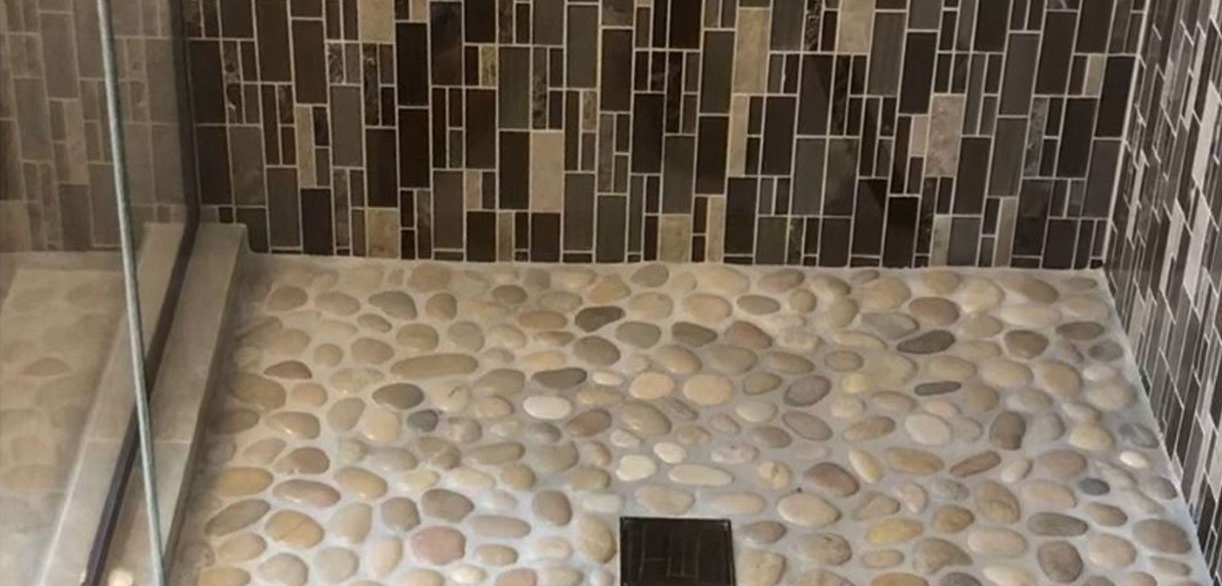 A walk in shower with a tiled floor and a glass door. Auckland Tilers