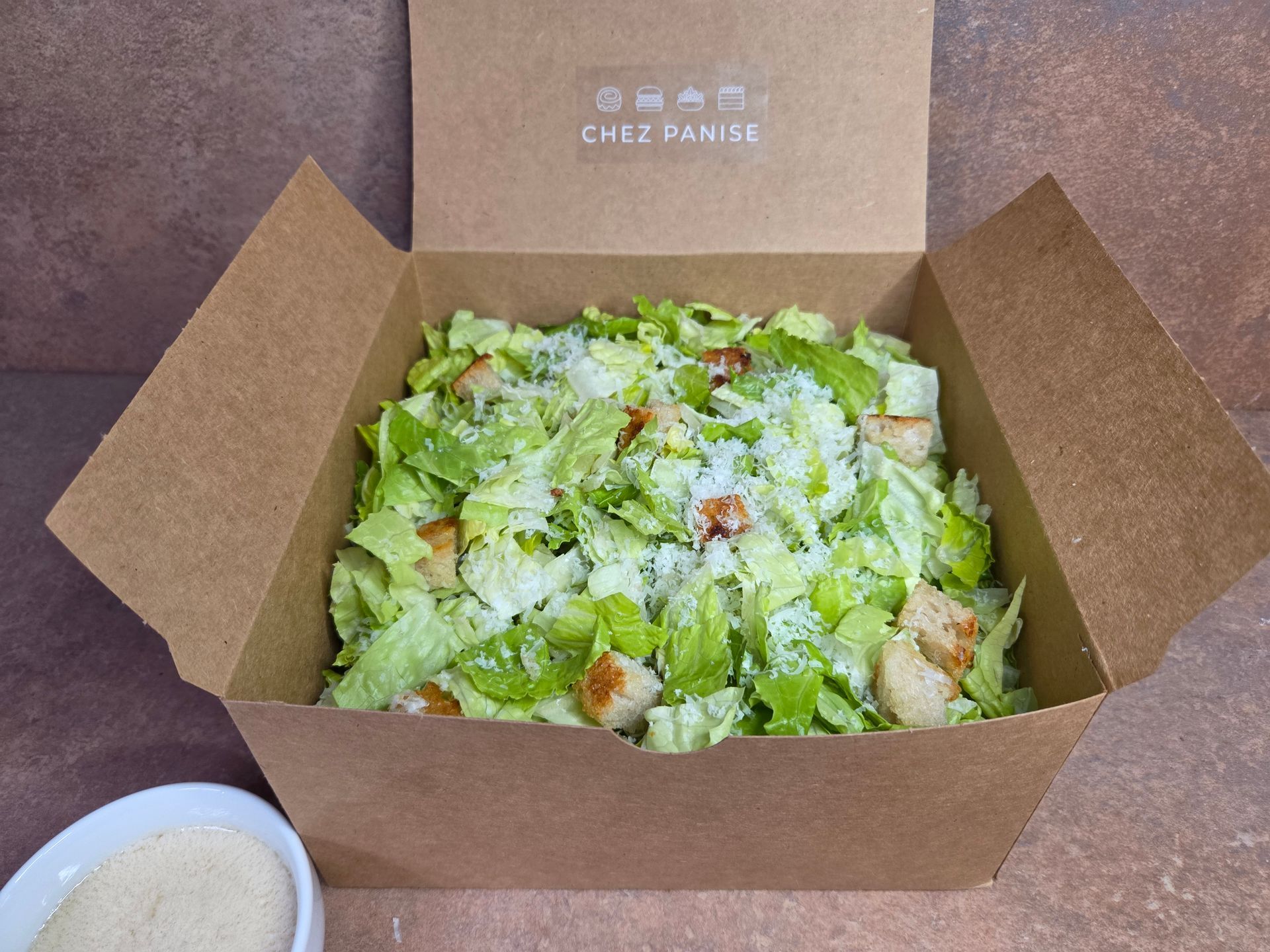 Chez panise large order of a Caesar salad in a brown box with a side of dressing