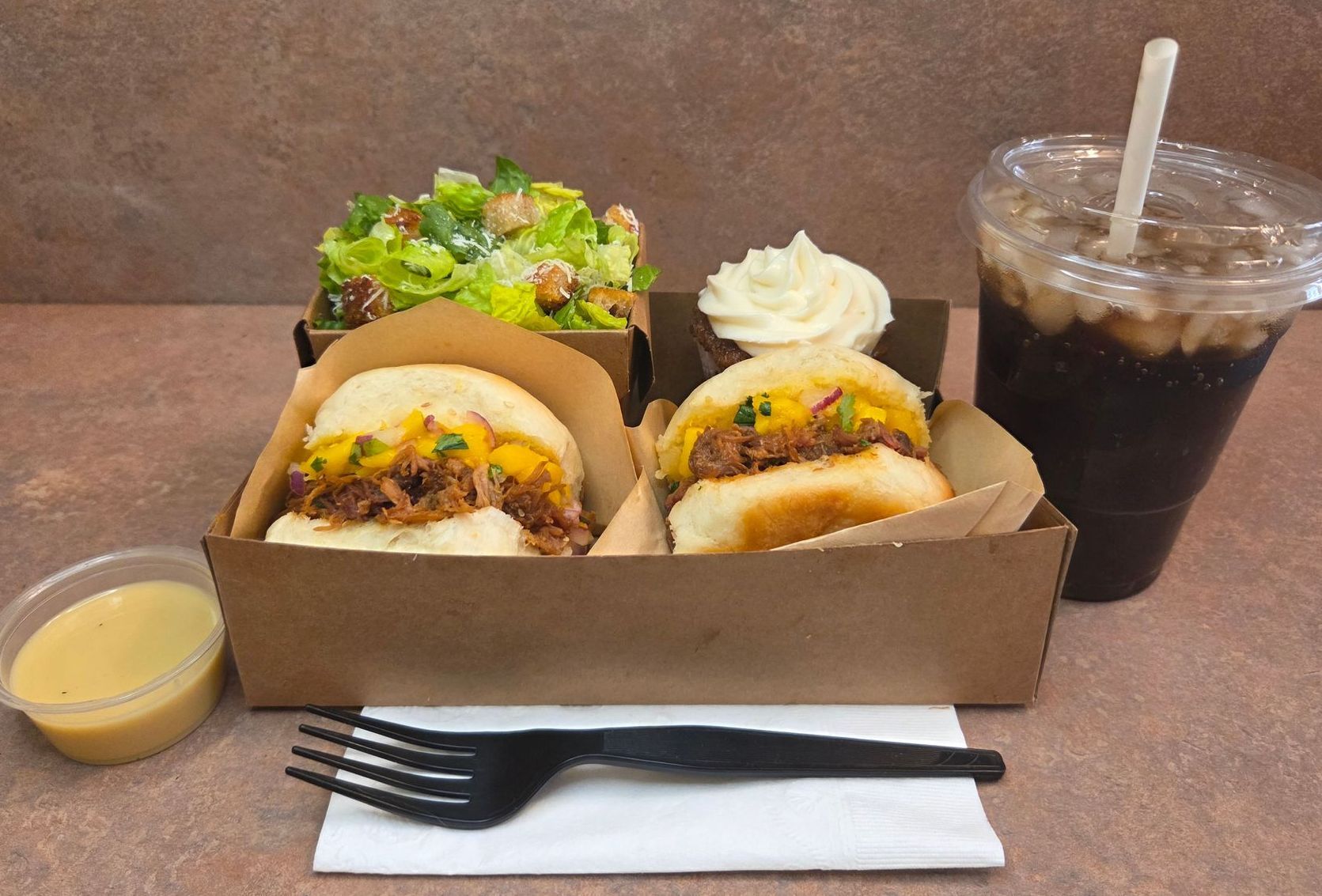 Chez Panise Number 3 Combo with 2 sliders, a salad, a drink, cupcake, and salad dressing with a fork and napkin