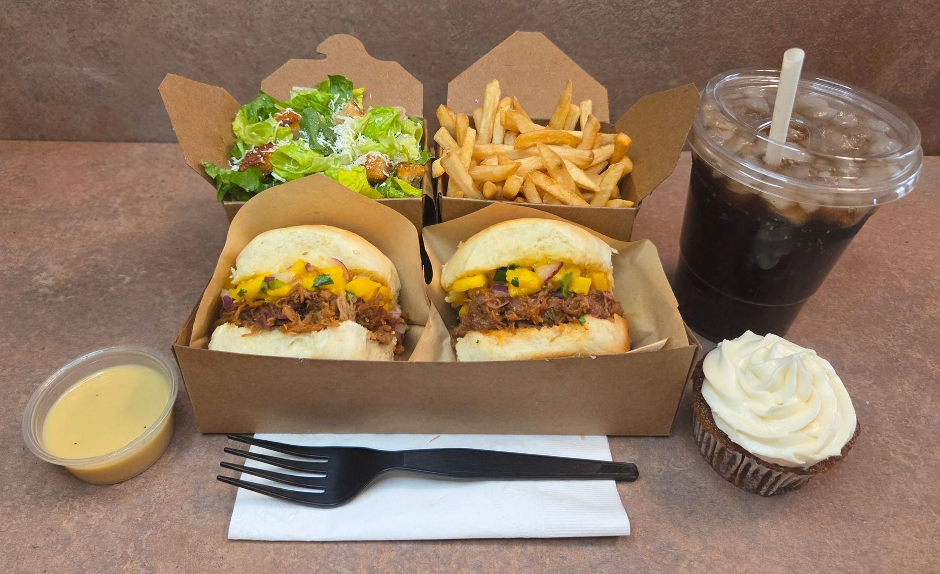 Chez Panise Number 4 Combo with 2 sliders, a salad, fries, a drink, cupcake, and salad dressing with a fork and napkin