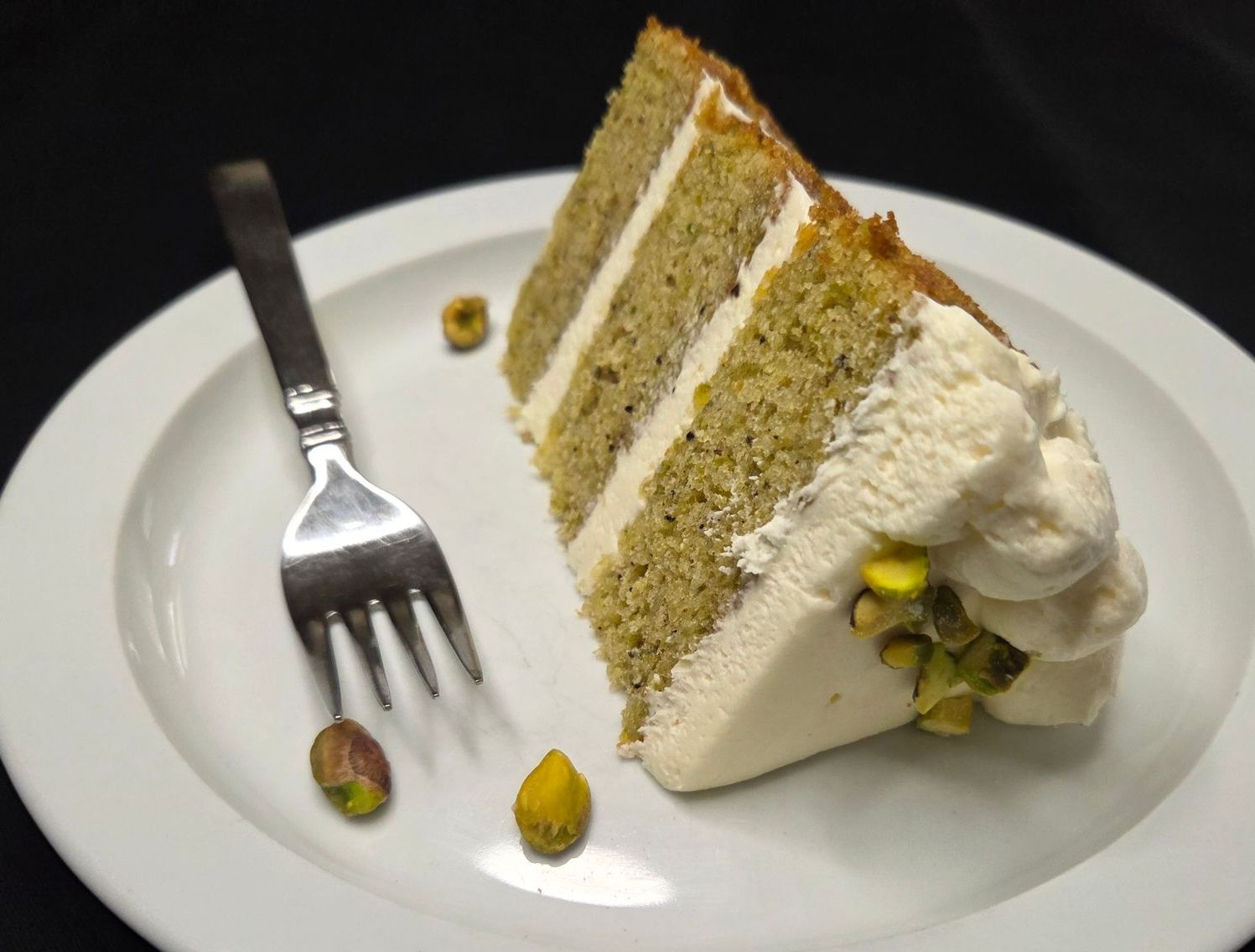 Slice of Chez Panise's Pistachio cake on a plate with a fork