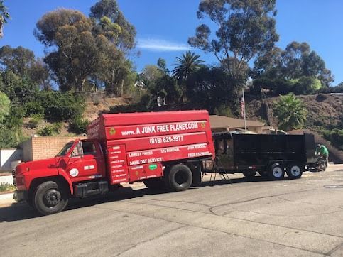 Red junk removal truck with trailer parked on a street near a house on a sunny day.