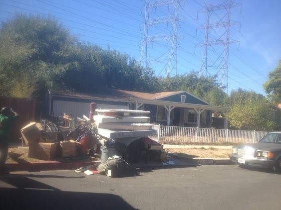 Pile of discarded items on a residential street in front of a house, possibly a move-out scene.
