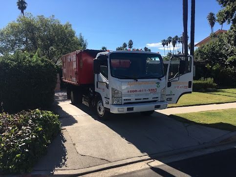 White truck with red bed parked on a driveway in front of a house. Door is open.