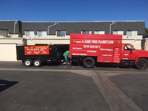 Red truck and black trailer used for junk removal with person loading items. Building in background.