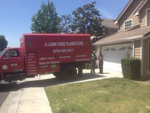 Red junk removal truck parked in front of a house; two people stand near truck.