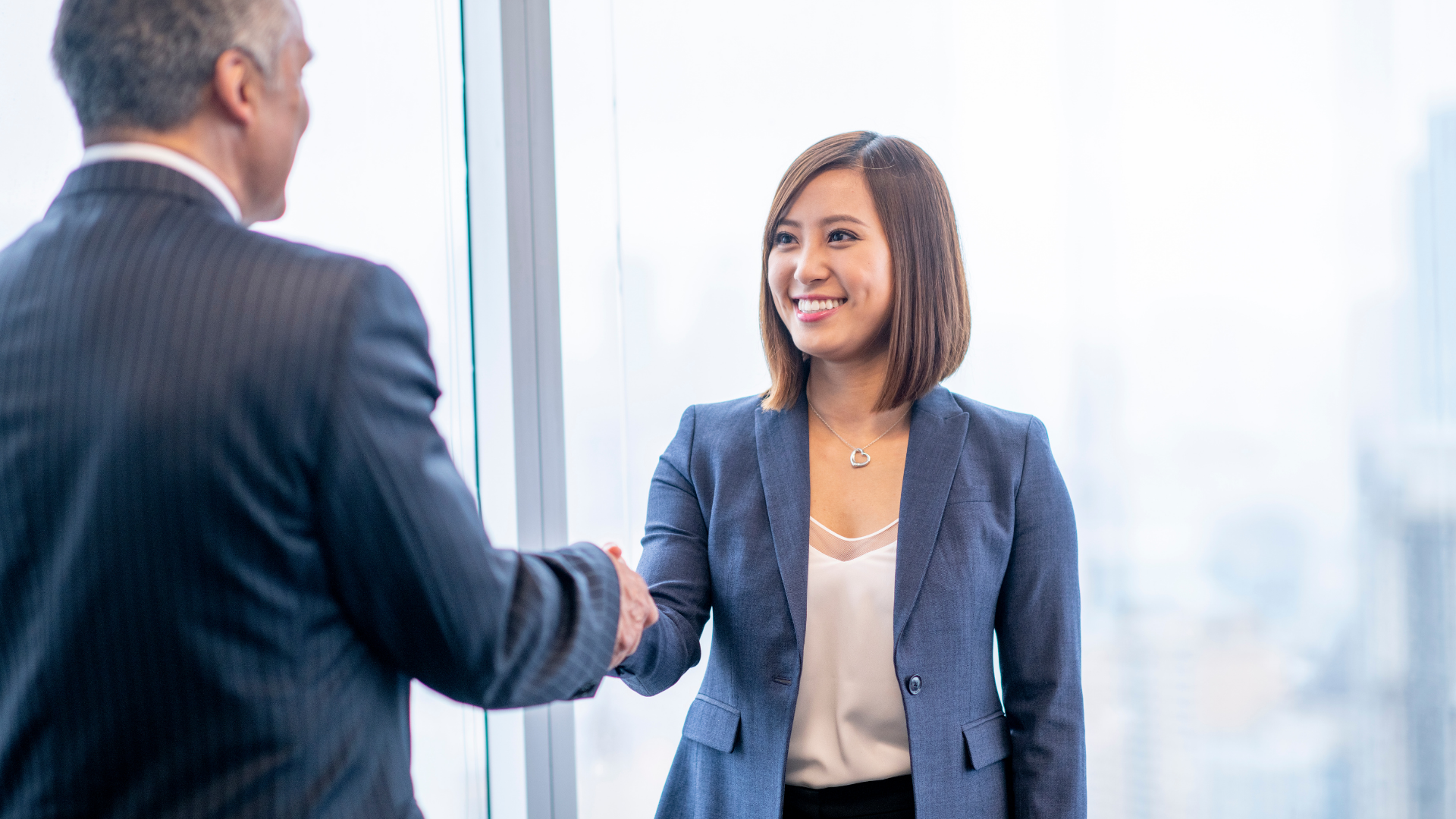A man and a woman are shaking hands in front of a window.
