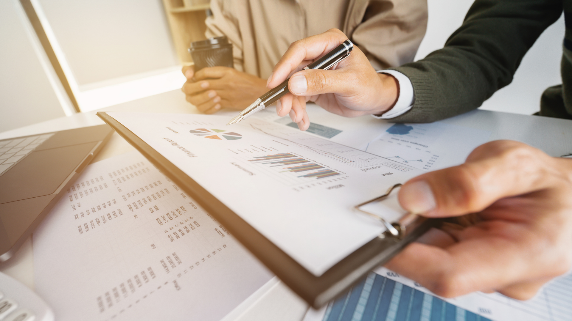 Two people reviewing financial reports at a desk. One person points with a pen.