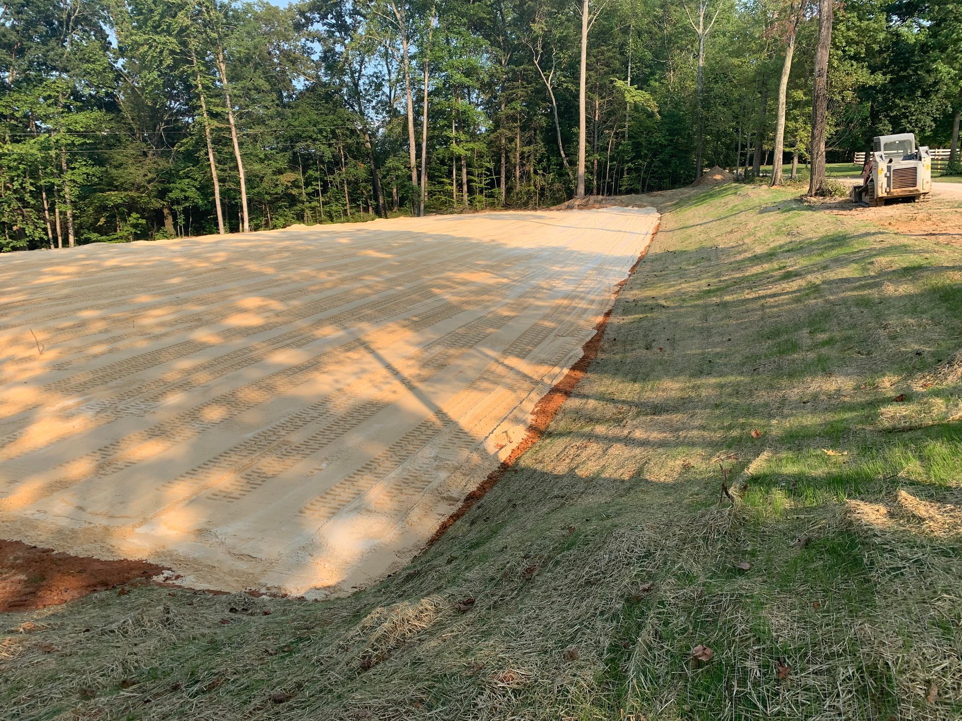 A dirt road going through a grassy field with trees in the background.