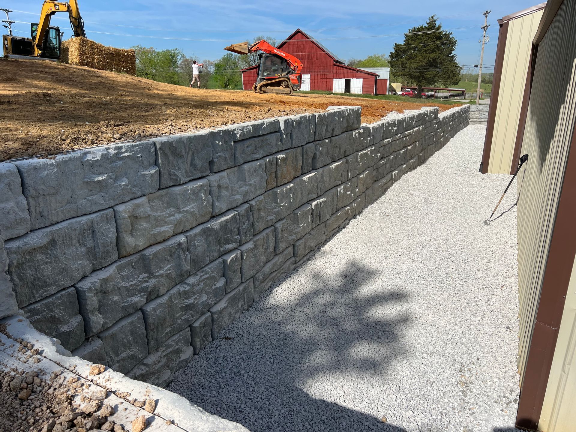 A brick wall is being built in front of a red barn.