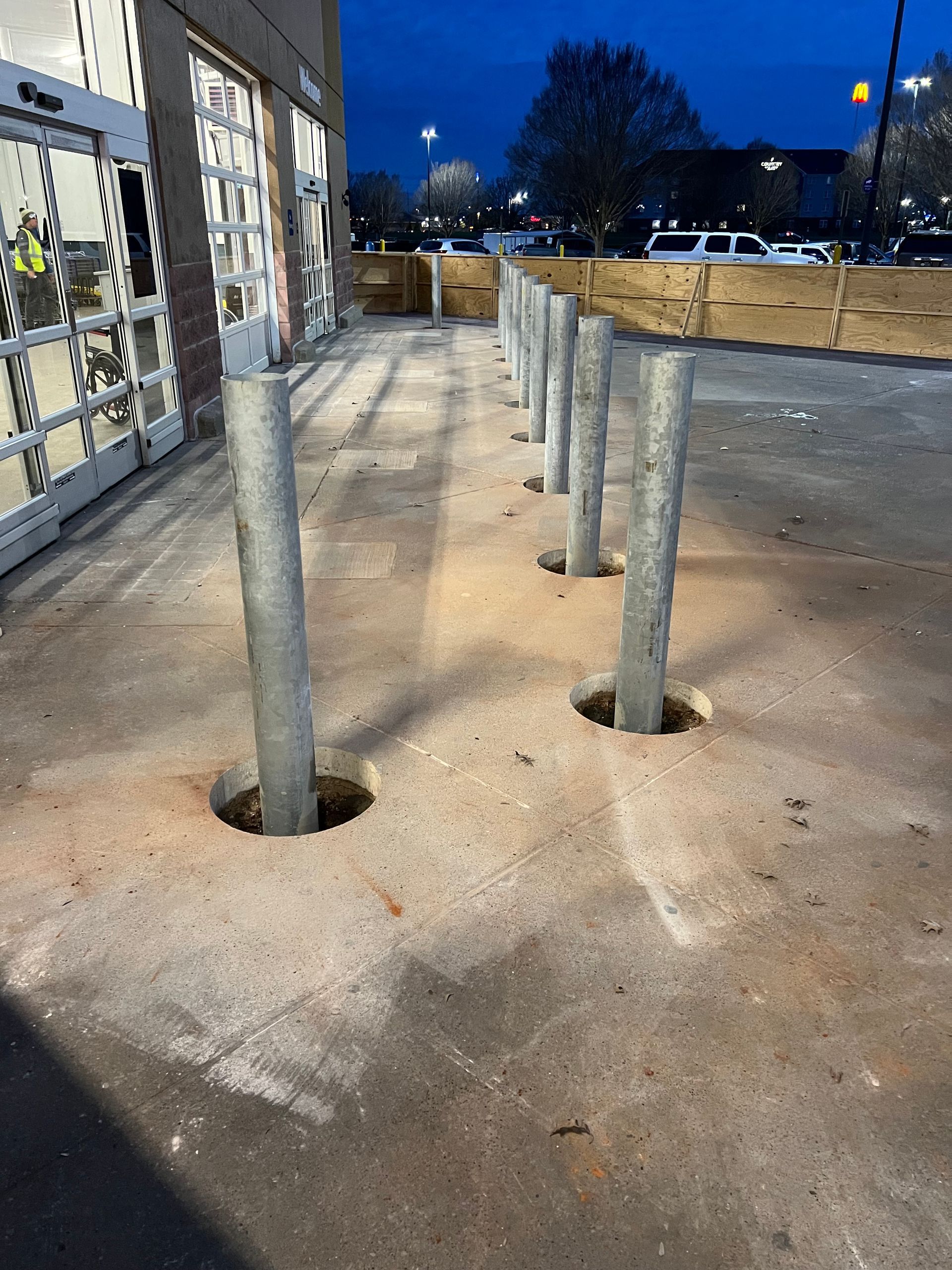 A row of concrete poles are sitting in the dirt in front of a building.