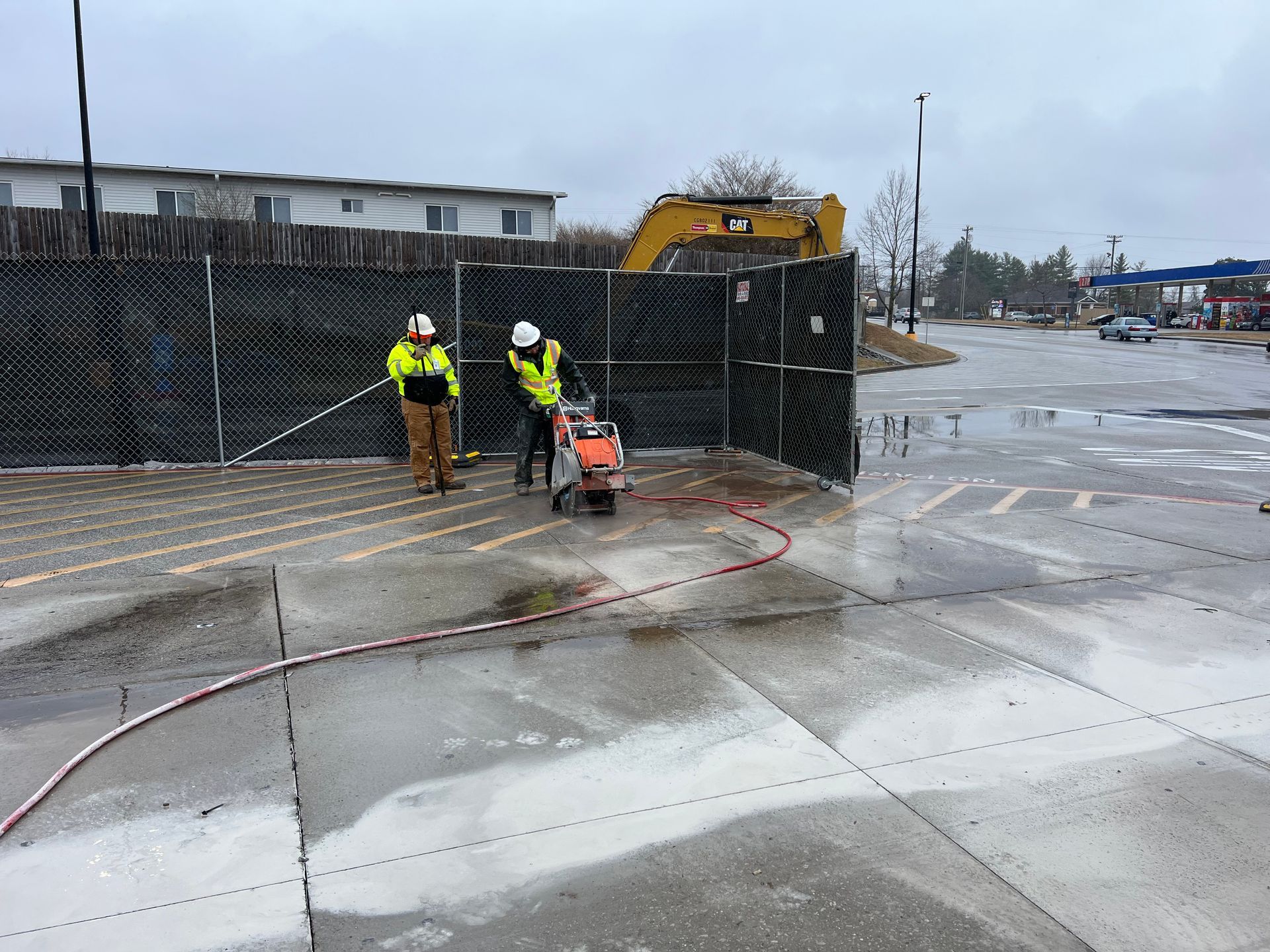 Two construction workers are cutting concrete in a parking lot.