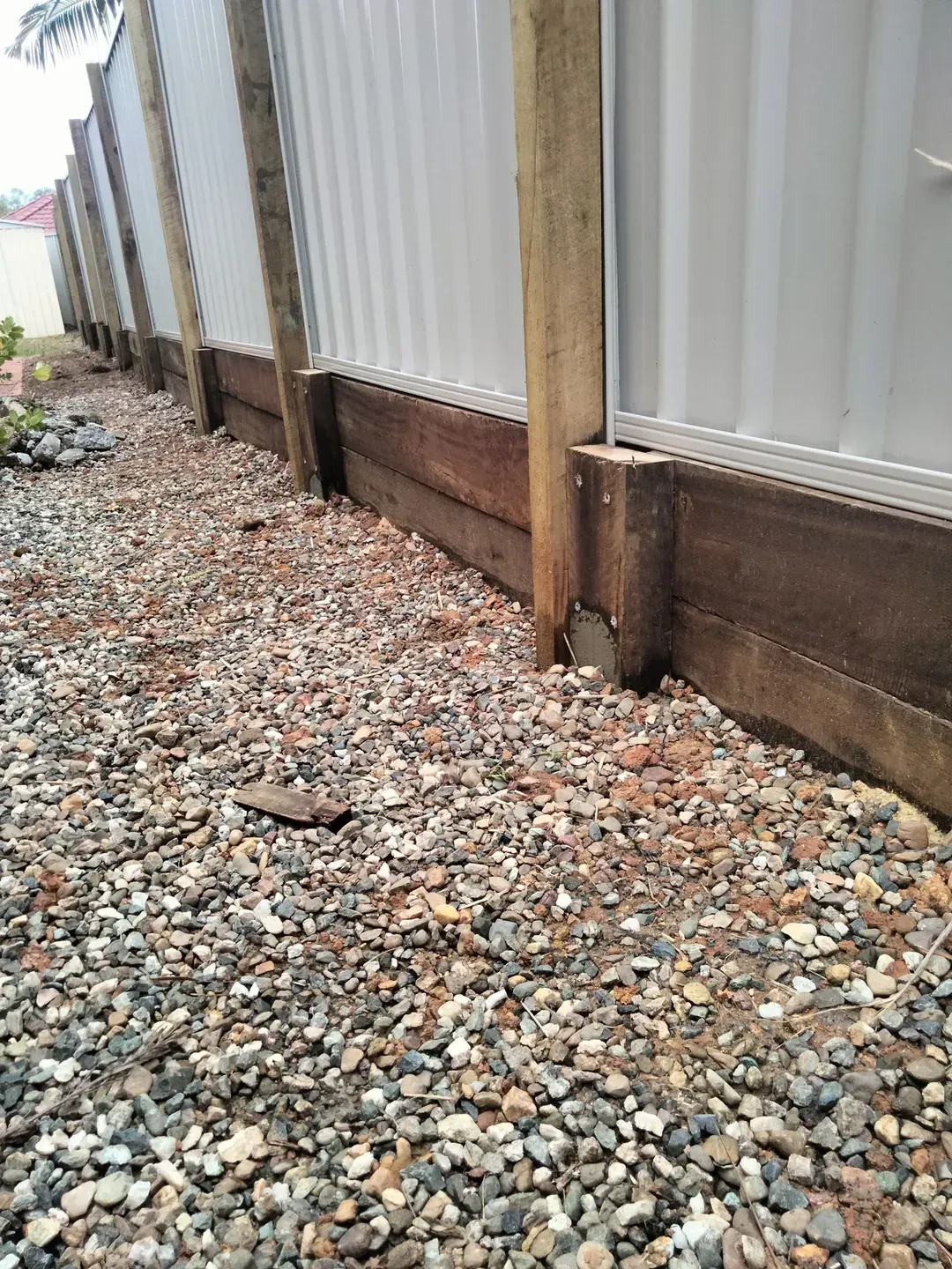 A Wooden Sleeper Retaining Wall is Surrounded by Gravel — Tuff Fencing in Burpengary, QLD