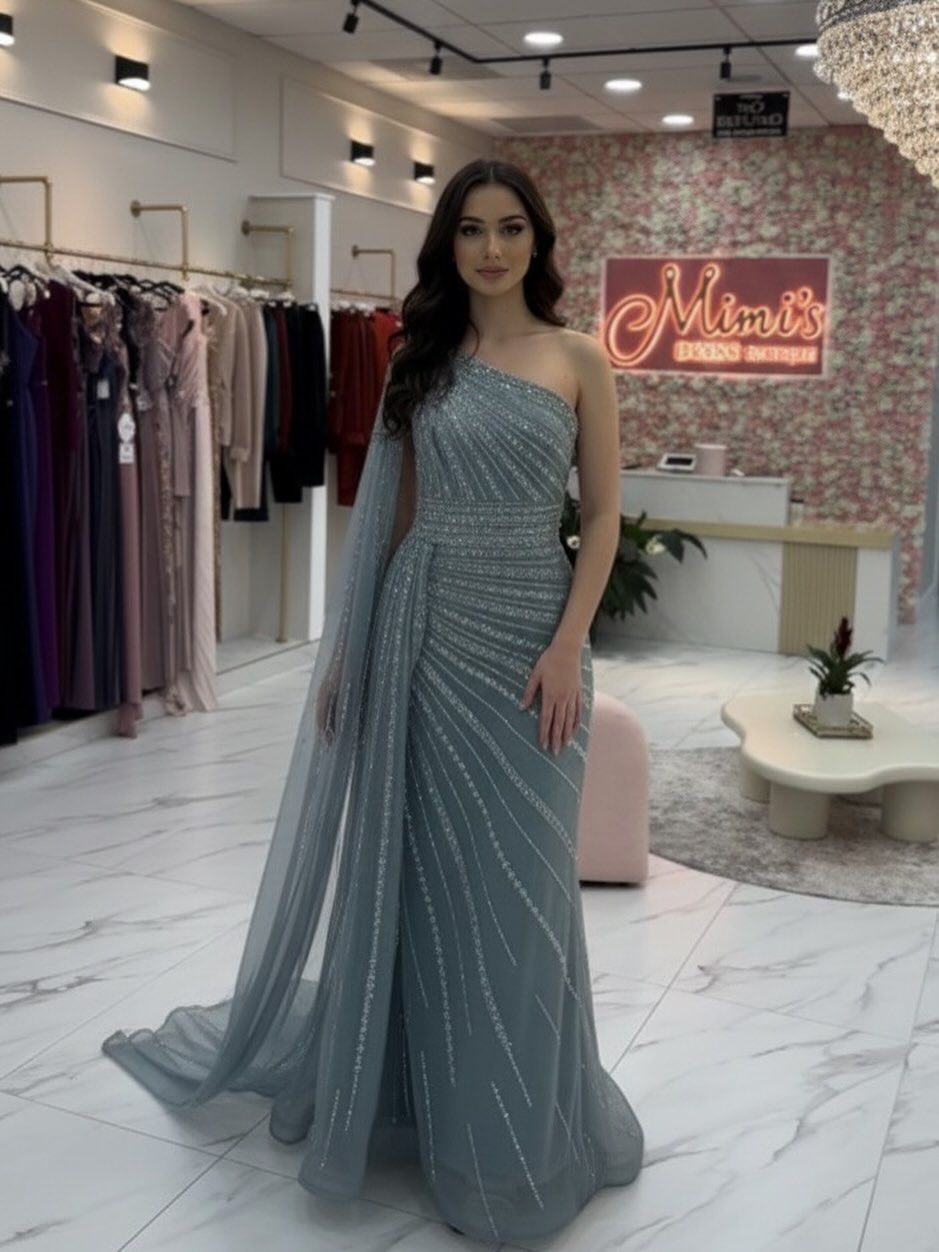 Woman in gold gown, standing in clothing store; dress has long sleeves, sparkles, and a sheer overlay.