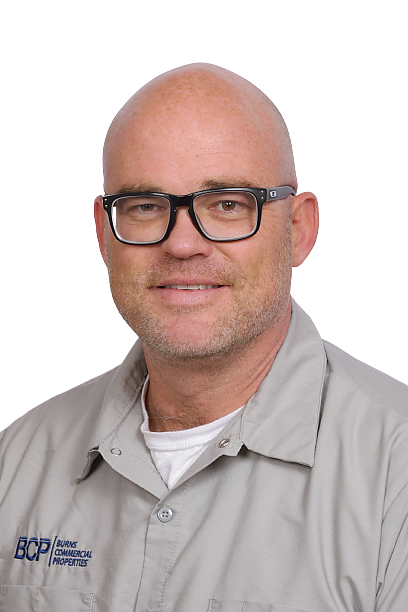 Portrait of a smiling bald man wearing black glasses and a gray collared shirt on a white background