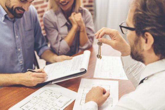 Business meeting with three people reviewing documents at a desk, one holding up a keychain.