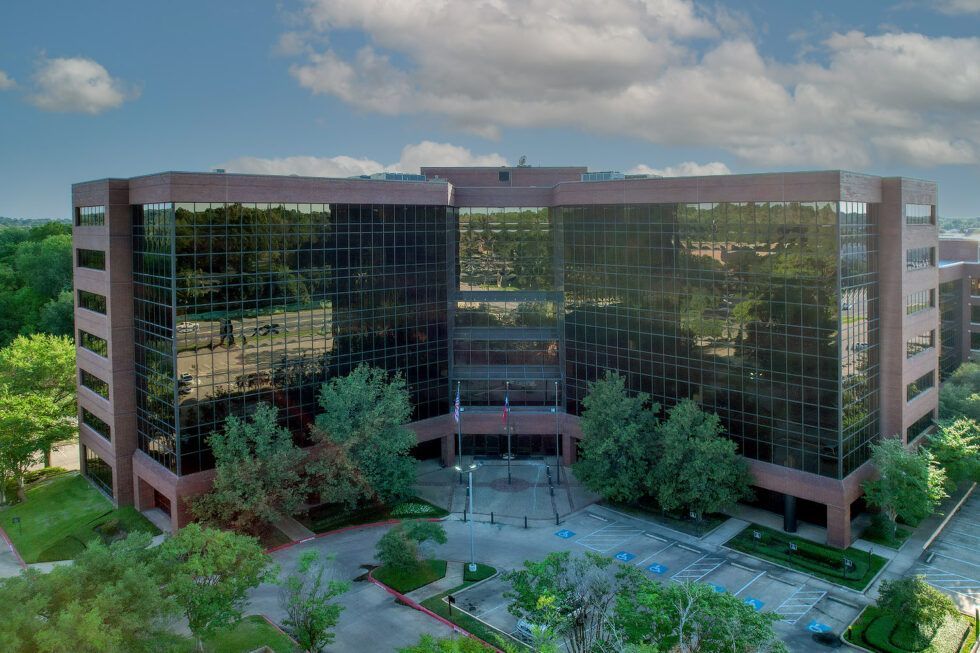 Modern glass office building with reflective windows and trees in front
