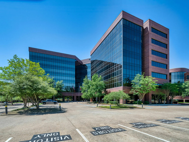 Modern office buildings with reflective glass under a clear blue sky, viewed from a parking lot.